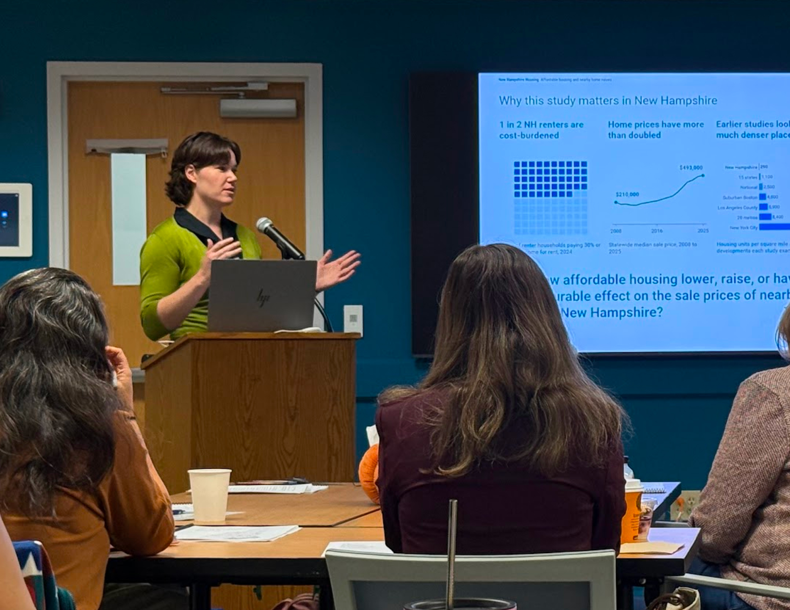 Presenter at a podium addressing a seated audience, with a slide titled 'Why this study matters in New Hampshire' projected on the screen.